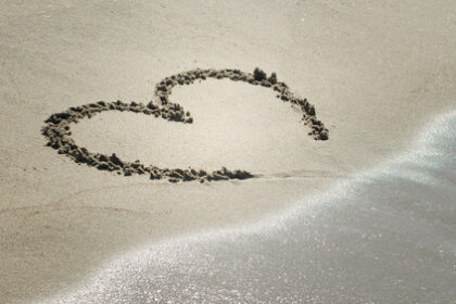 Handwritten heart on sand with wave approaching